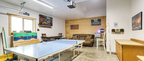 A room with a ping pong table, a wooden sofa, and a television mounted on the wall.