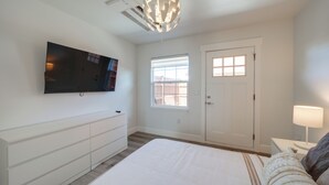 A bedroom with a bed, a TV mounted on the wall, a window, and a door. - Private Patio, Steps to Lake: Soap Lake Studio! (Soap Lake)