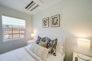 A bedroom with a bed, two bedside lamps, a window, and a wall-mounted air conditioner. - Walk to Water: Soap Lake Studio w/ Patio! (Soap Lake)