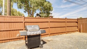 Un barbecue portatif doté de quatre brûleurs, placé sur une surface de gravier, avec une clôture en bois et des arbres en arrière-plan.