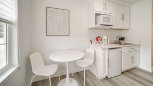 Une cuisine moderne avec des meubles blancs, un four à micro-ondes, une machine à café et un évier. On y trouve une petite table ronde accompagnée de deux chaises.