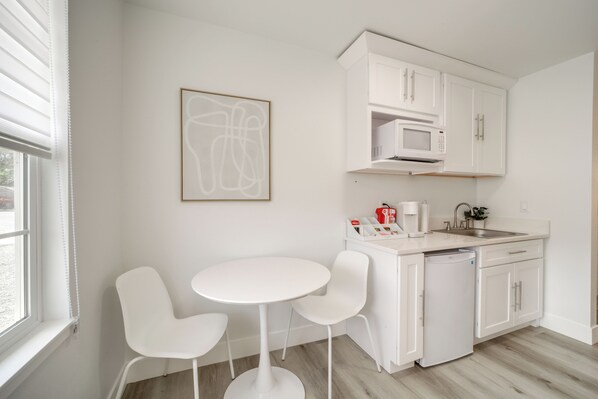 A modern kitchen with white cabinetry, a microwave, a coffee machine, and a sink. There is a small round table with two chairs.