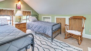 Une chambre à coucher avec deux lits, un fauteuil à bascule en bois, une lampe et une fenêtre avec des rideaux.