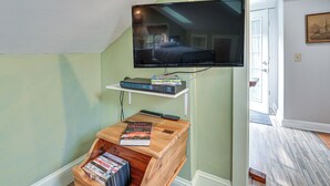 Une chambre à coucher avec un téléviseur fixé au mur, une table de chevet avec des livres et une commode en bois.
