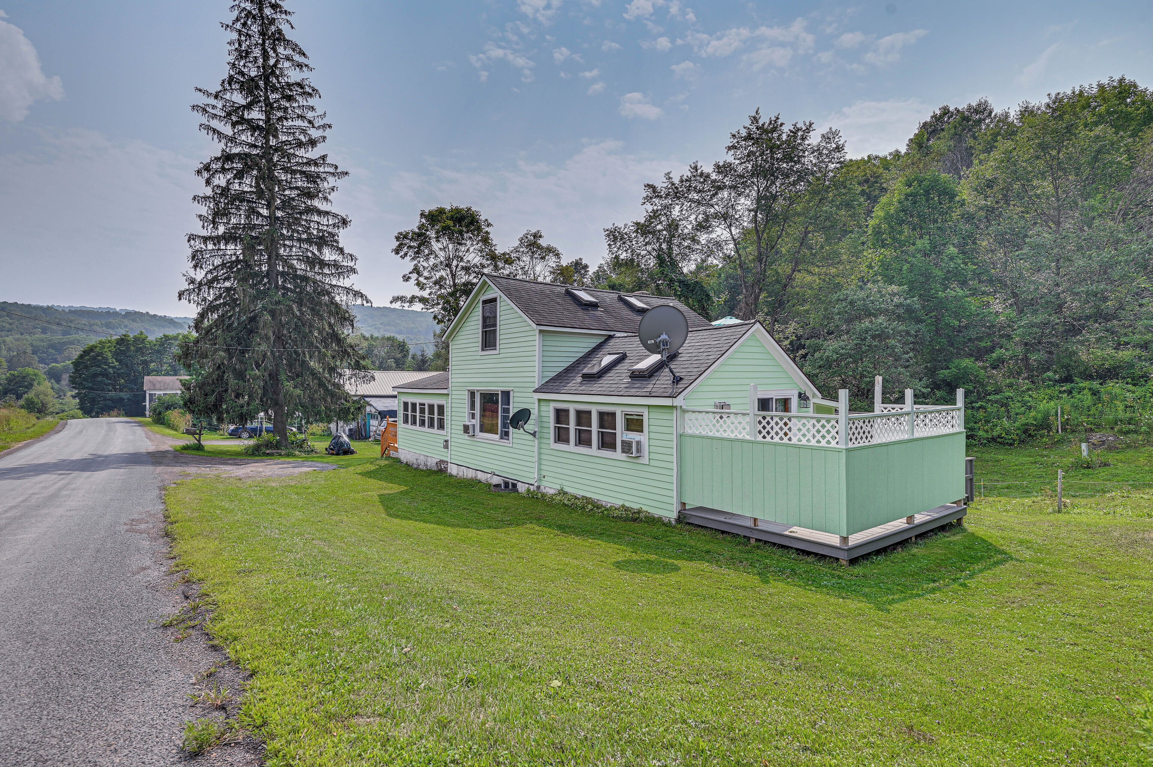 A light green house with a fenced deck, a satellite dish, and a large tree nearby.