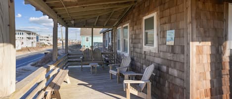 A wooden deck with Adirondack chairs and a bench, overlooking a road with buildings in the background.
