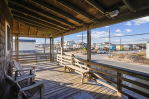 Eine Holzterrasse mit Bänken, die auf einen Strand mit Häusern und einer Straße hinausblickt.
