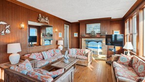 A cozy living room with wooden paneling, a fireplace, and a large TV.