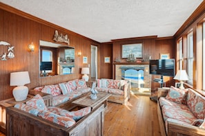 A cozy living room with wooden paneling, a fireplace, and a large TV.