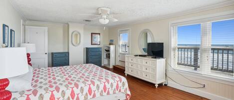 A bedroom with a bed, dresser, and a television. There is a window with a view of the ocean.