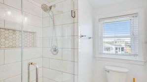 A bathroom with a glass-enclosed shower, a toilet, and a window with blinds.