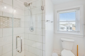 A bathroom with a glass-enclosed shower, a toilet, and a window with blinds.