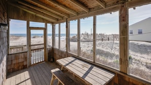 A wooden beach house with a large window overlooking the beach and ocean.