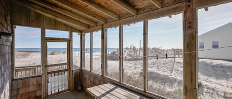 A wooden beach house with a large window overlooking the beach and ocean.