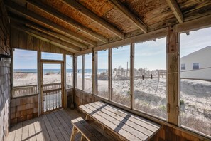 A wooden beach house with a large window overlooking the beach and ocean.