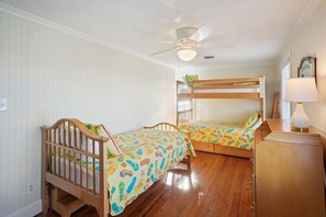 Une chambre avec deux lits superposés, un ventilateur de plafond, une lampe et un panneau fixé au mur.