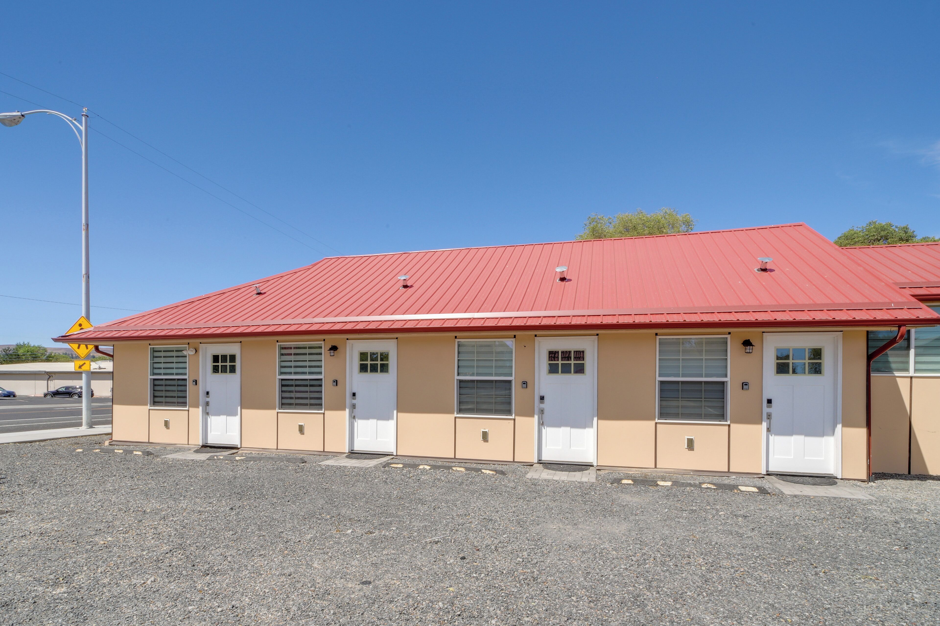 A single-story building with a red roof and beige walls, featuring four doors and windows, located in a parking lot.