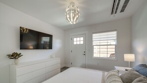 A bedroom with a bed, a dresser, a TV mounted on the wall, a door, a window with blinds, and a bedside lamp. - Steps to Soap Lake: Studio Stay w/ Patio! (Soap Lake)