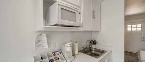 Una cocina moderna con armarios blancos, microondas integrado, cafetera y lavaplatos.