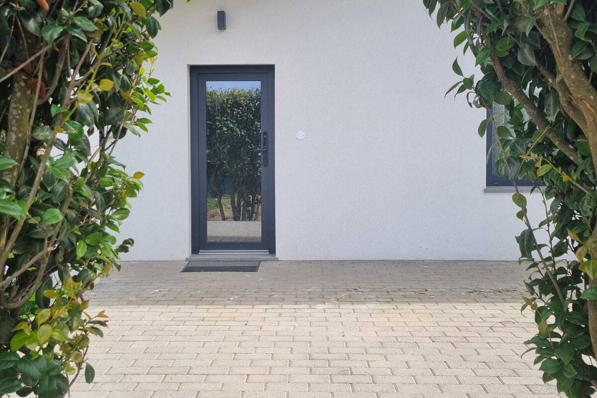 Un edificio moderno con una puerta negra, un ventanal pequeño y una zona de entrada pavimentada.