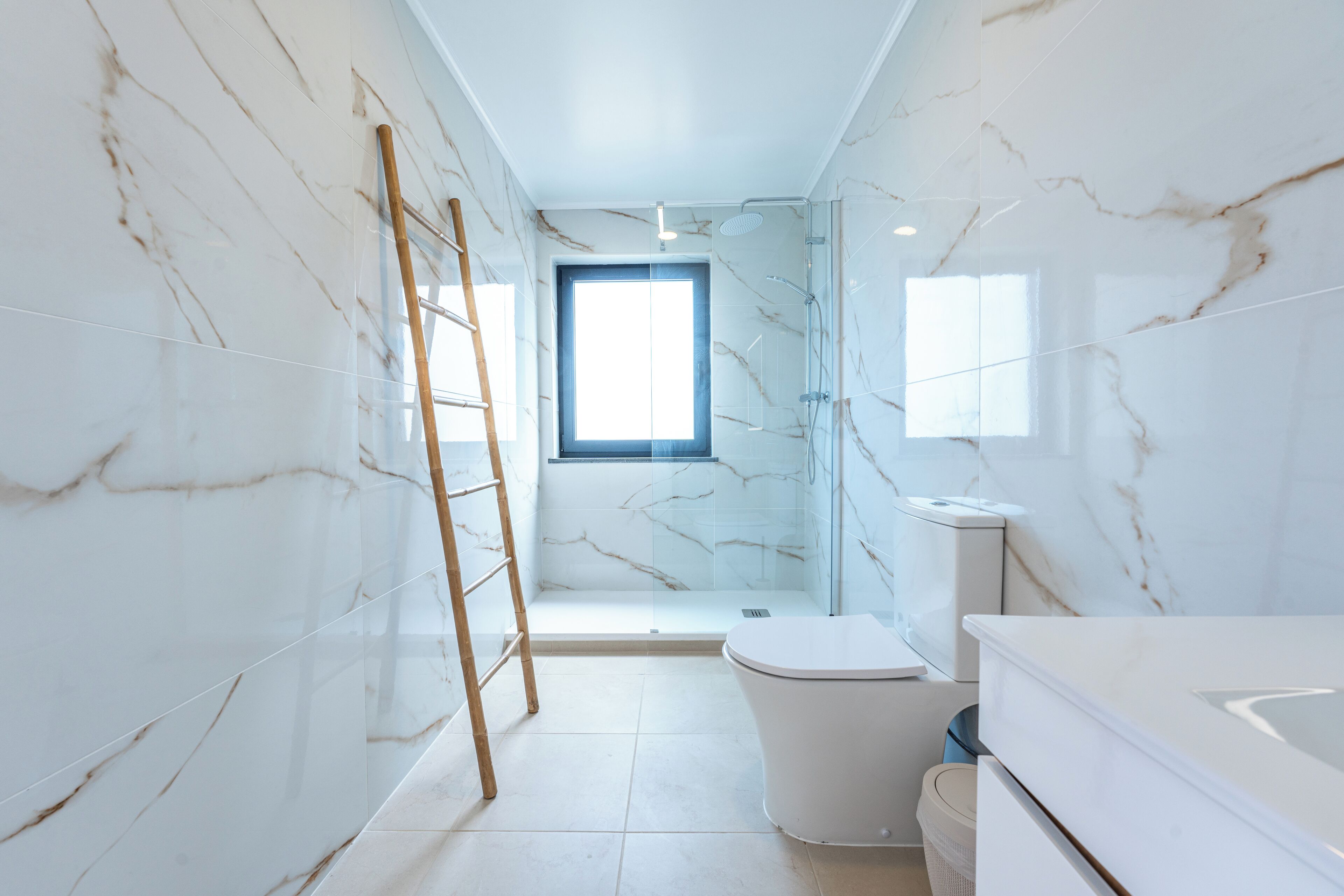 A bathroom with marble walls, a toilet, a shower, and a window.