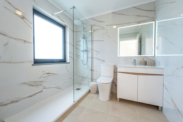 A modern bathroom with a glass-enclosed shower, a toilet, a sink with a mirror, and marble walls.