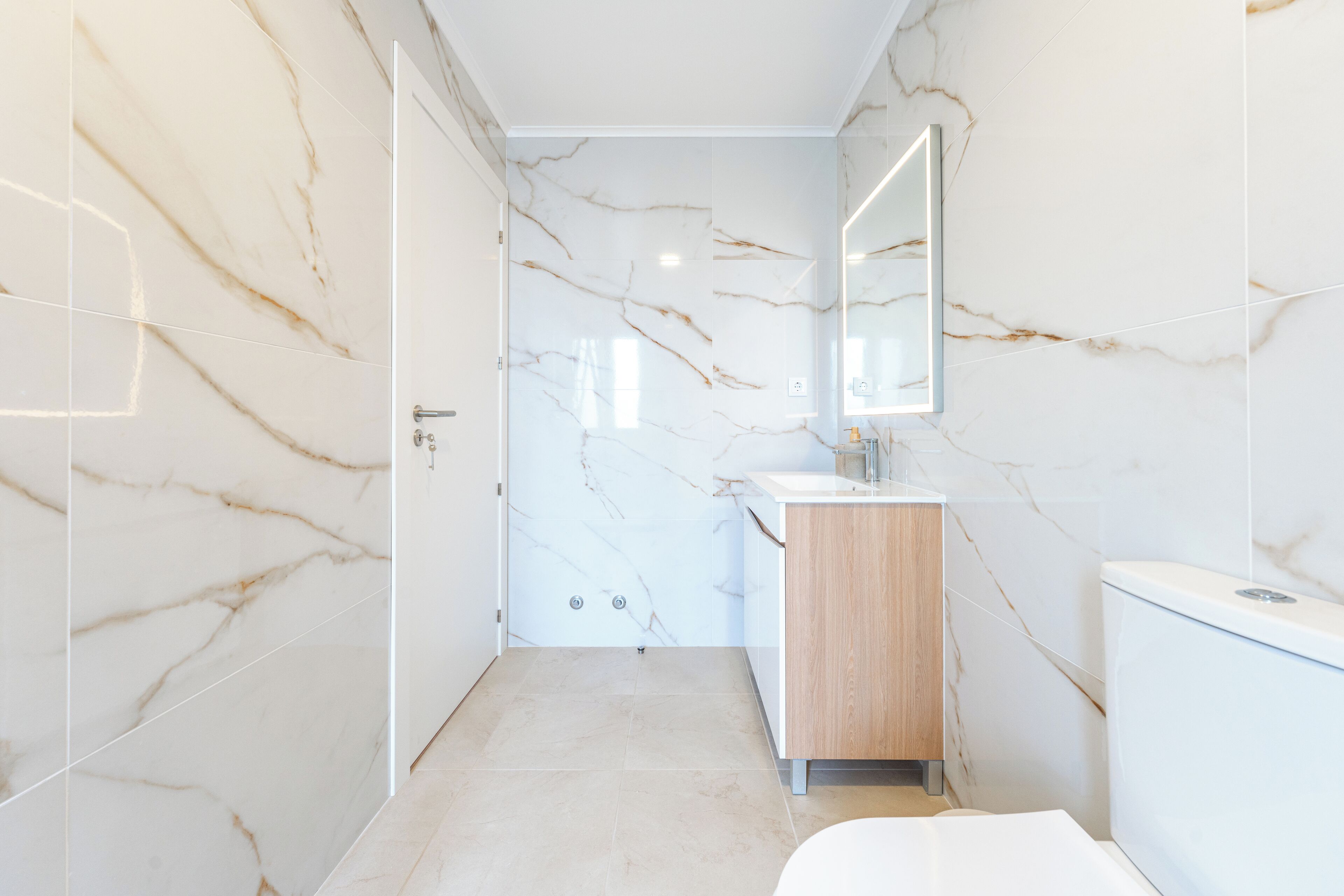 A modern bathroom with marble walls and a wooden vanity.
