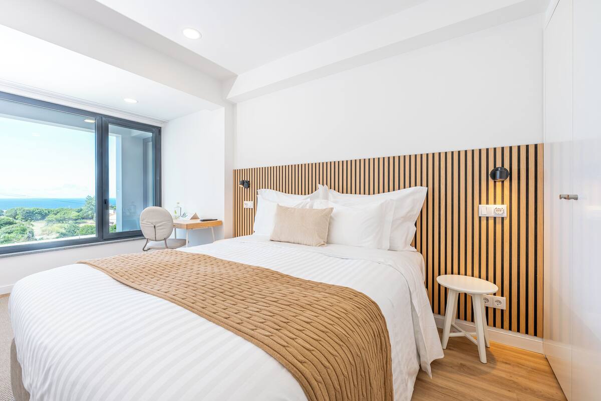 Un dormitorio moderno con una cama grande, un cabecero de madera, una mesita de noche y vistas al exterior.