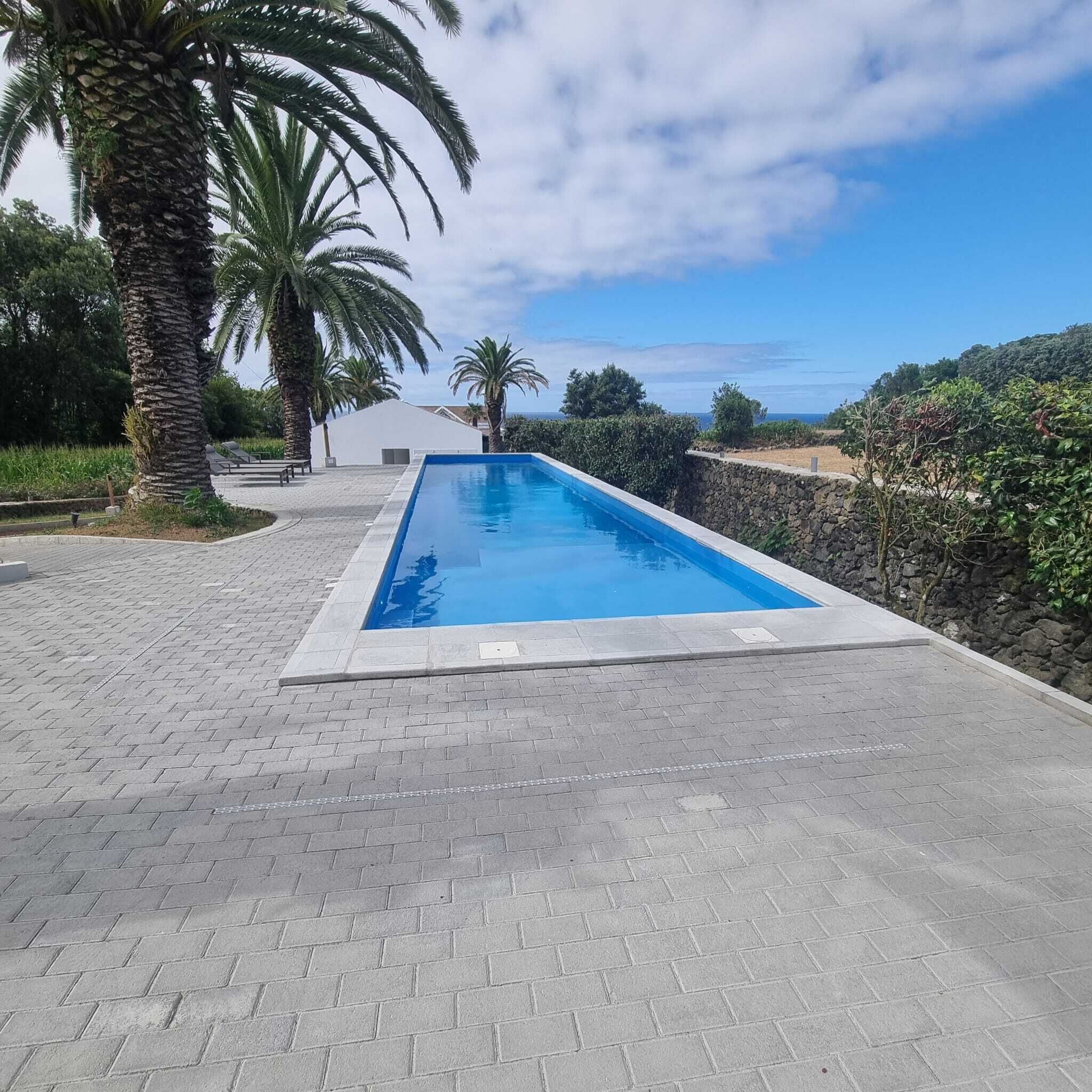 Ein rechteckiger Pool mit einer Steinmauer an einer Seite und einem gepflasterten Weg, der zu einem weißen Gebäude führt.