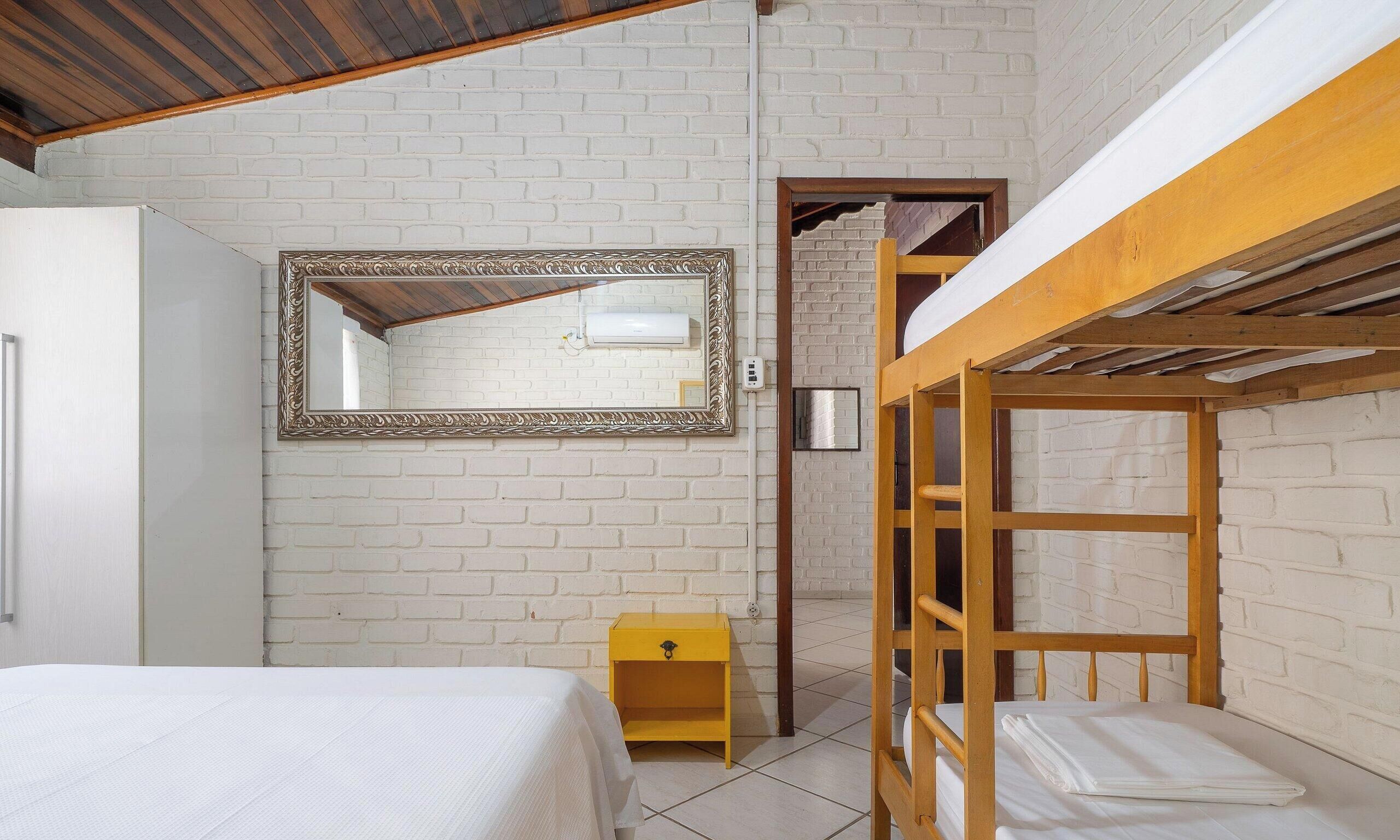 A room with a bunk bed, a single bed, a mirror, and a small yellow nightstand.
