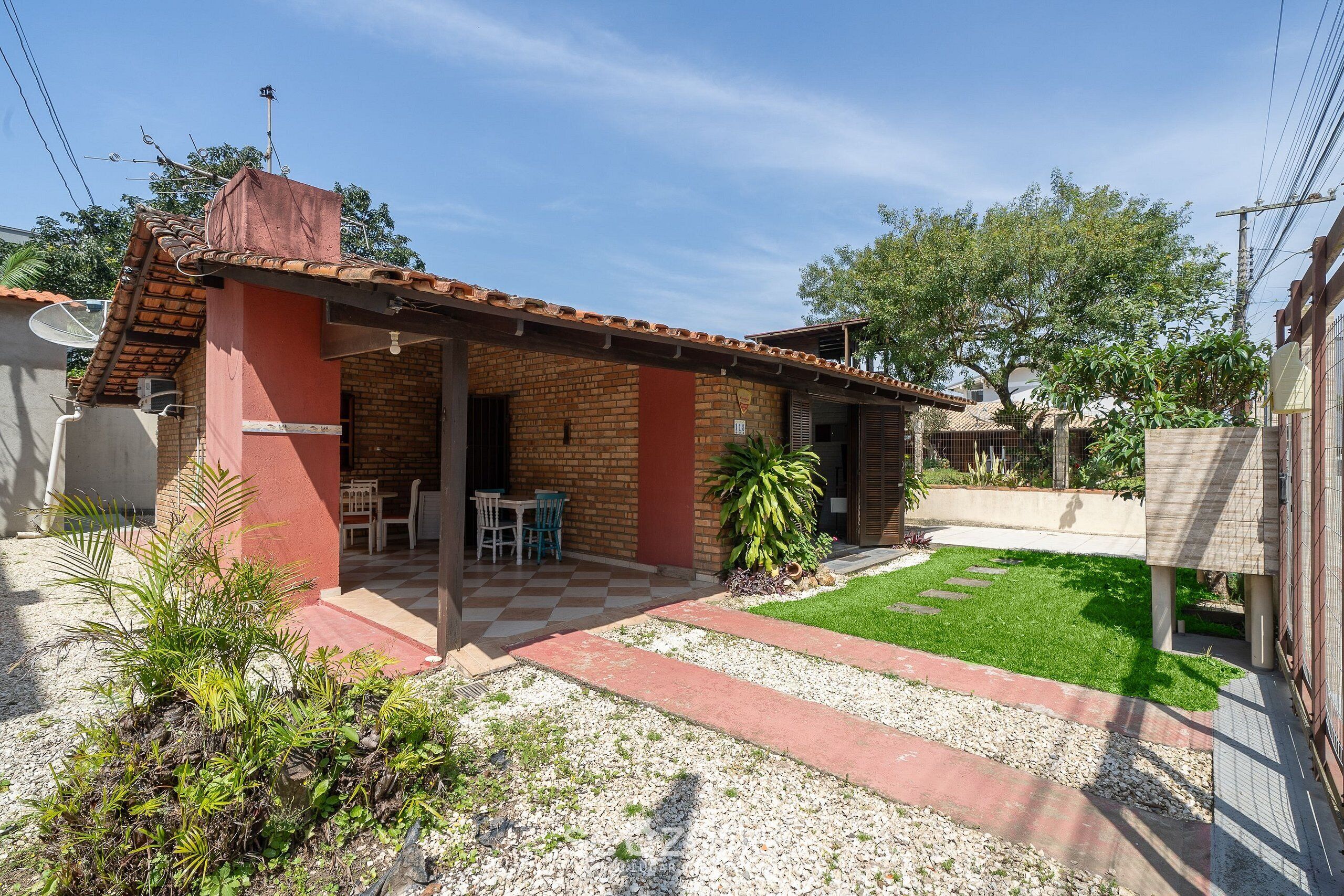 A small brick house with a tiled roof, a patio with a checkered floor, and a small garden area with plants and a lawn.