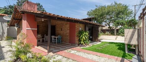A small brick house with a tiled roof, a patio with a checkered floor, and a small garden area with plants and a lawn.