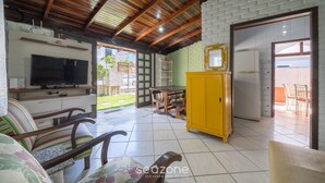 A spacious living area with a wooden ceiling, a TV, a yellow cabinet, and a dining table. - 3BR House 230m From Beach w/ BBQ & Grg Rgv115 (Bombinhas)
