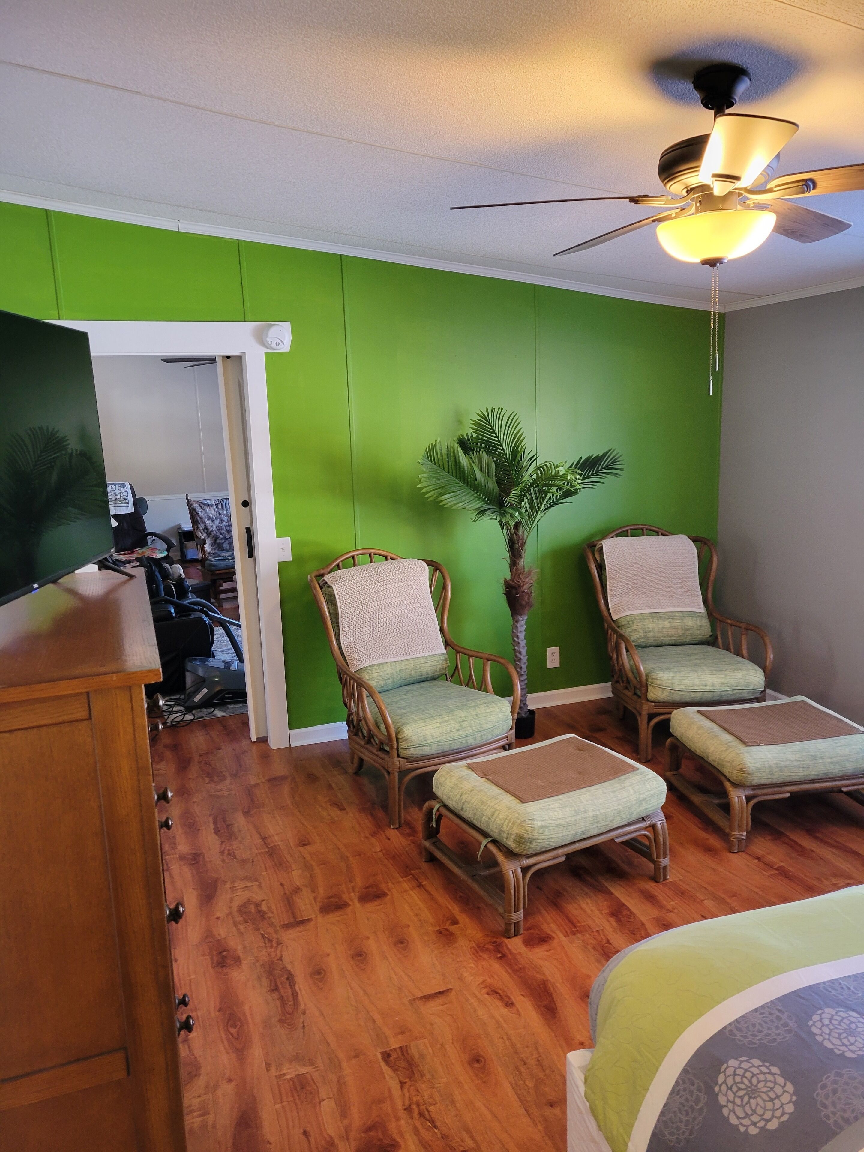 A room with green walls, a ceiling fan, wicker furniture, and a wooden floor.