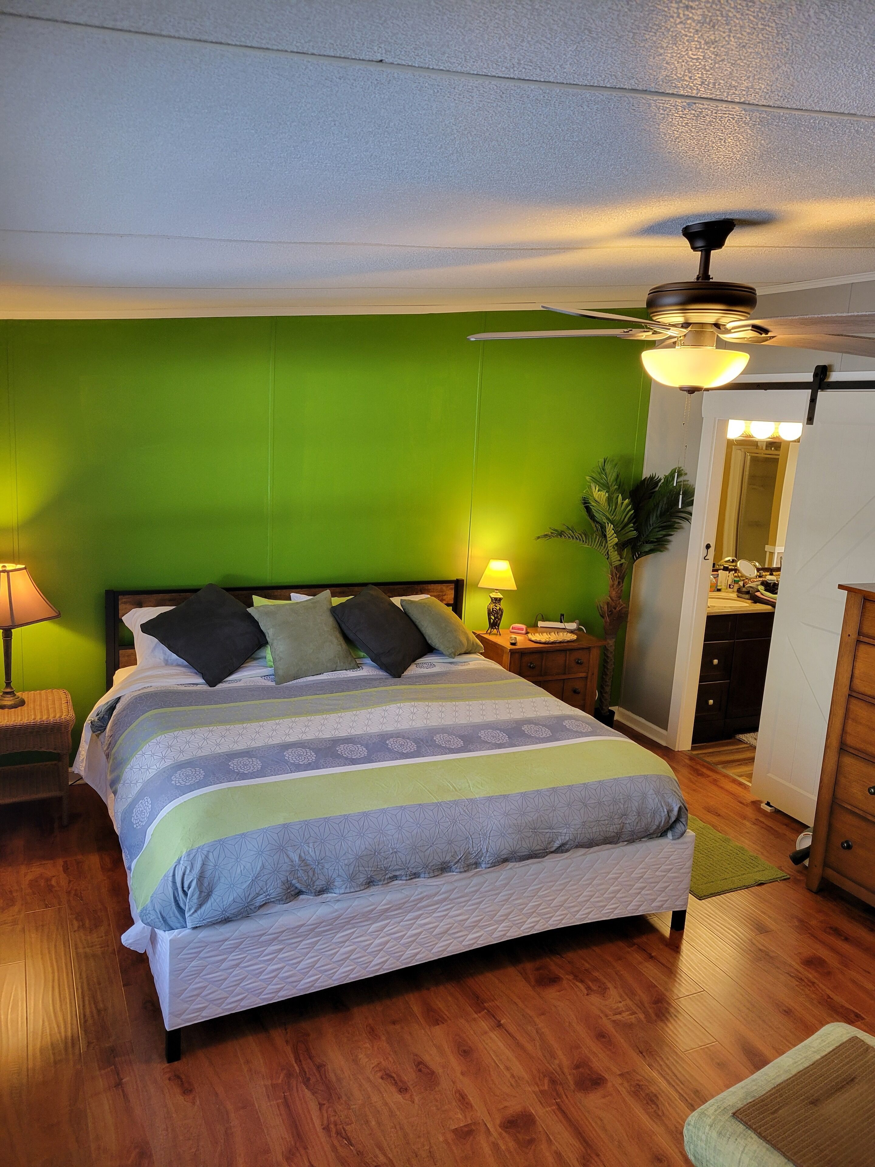 A bedroom with a bed, nightstands, a ceiling fan, and a green wall.