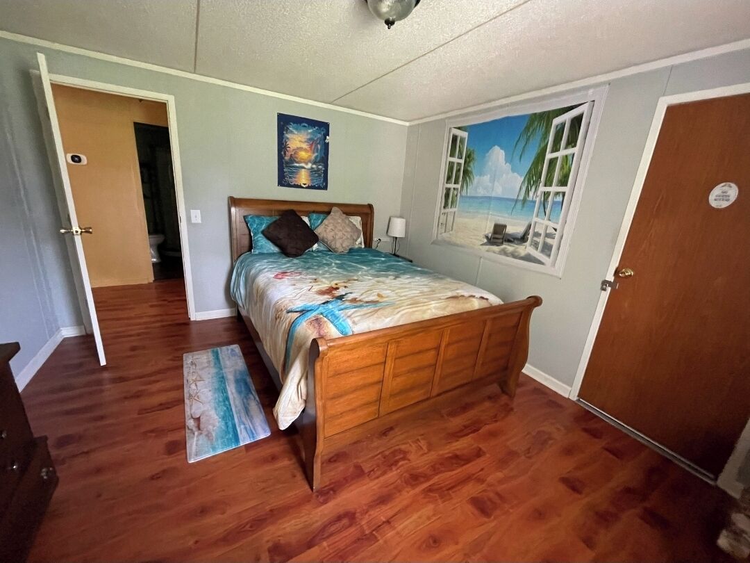 Un dormitorio con cama de madera, vista a la ventana con temática playera y puerta que conduce a otra habitación.
