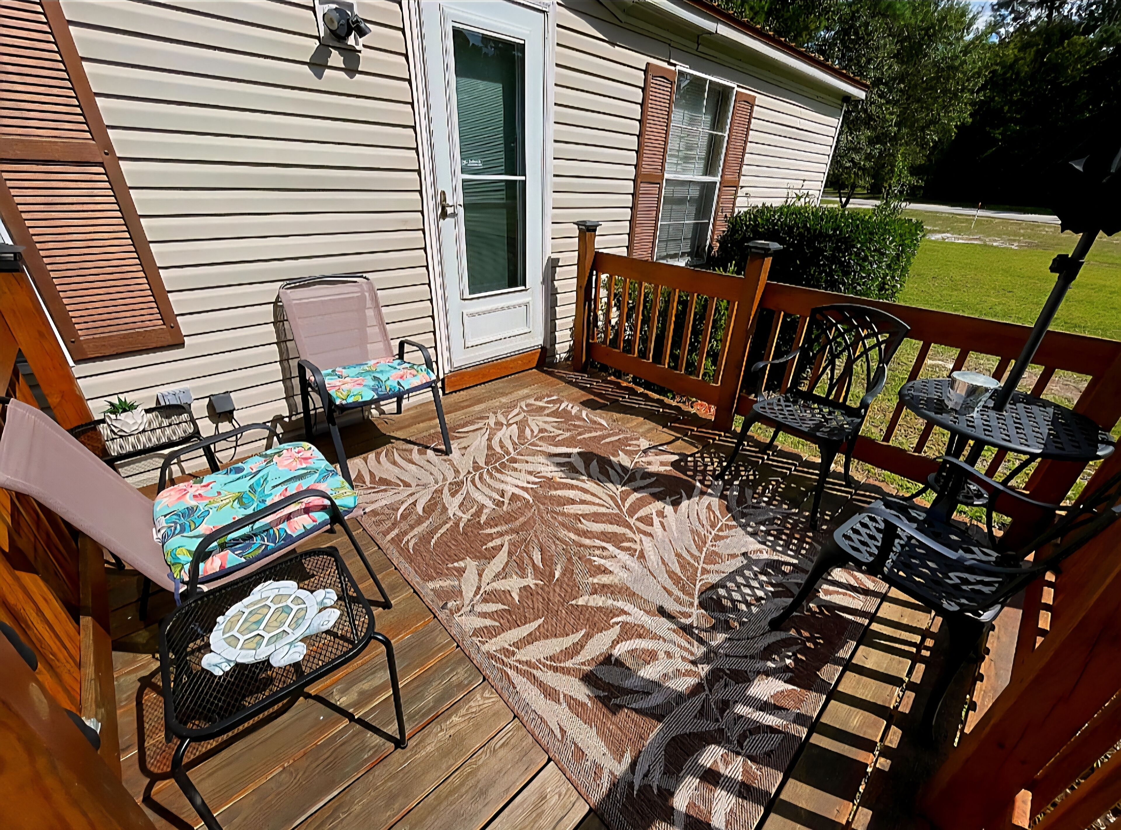 A wooden deck with outdoor furniture, including chairs and a table, and a patterned rug.