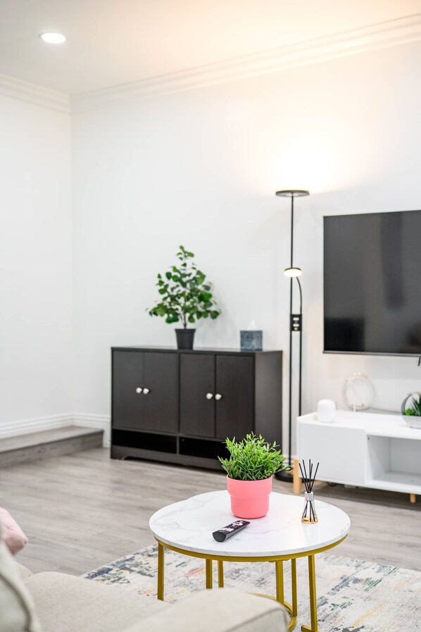 Uma sala de estar moderna com uma mesa redonda branca, um armário preto, uma planta em vaso e uma televisão na parede.