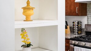 Une cuisine avec des étagères blanches, un pot jaune, un pot en bois et une plante en pot.