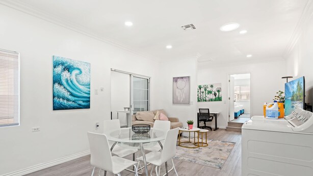 Un salon moderne avec une table à manger en verre, des chaises blanches, un canapé beige et un lave-linge blanc.