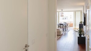 Un pasillo con una puerta blanca, suelo de madera y un comedor al fondo.