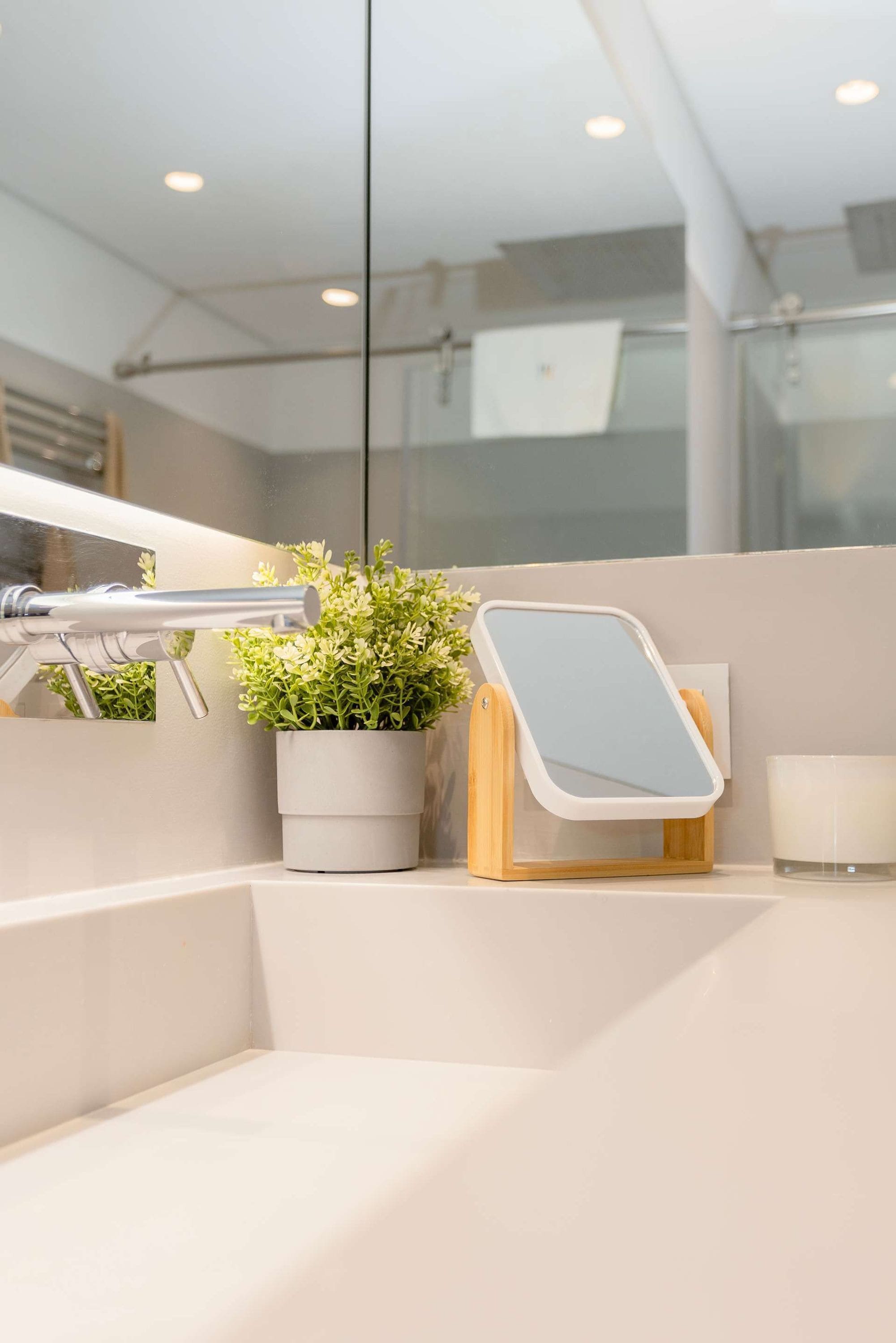 A bathroom with a mirror, a potted plant, and a candle on a counter.