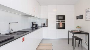 Una cocina moderna con armarios blancos, una encimera negra, una cafetera y un pequeño comedor con taburetes.