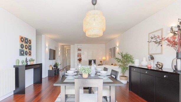 Una cocina moderna con comedor, que presenta un amplio tablero para cuatro personas, un armario negro y una lámpara colgante.