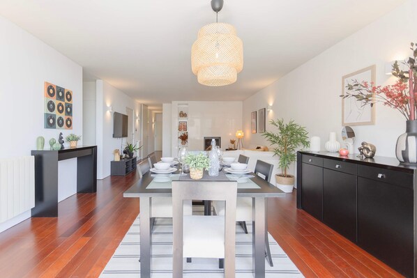 A modern kitchen with a dining area, featuring a large table set for four, a black cabinet, and a hanging light fixture.