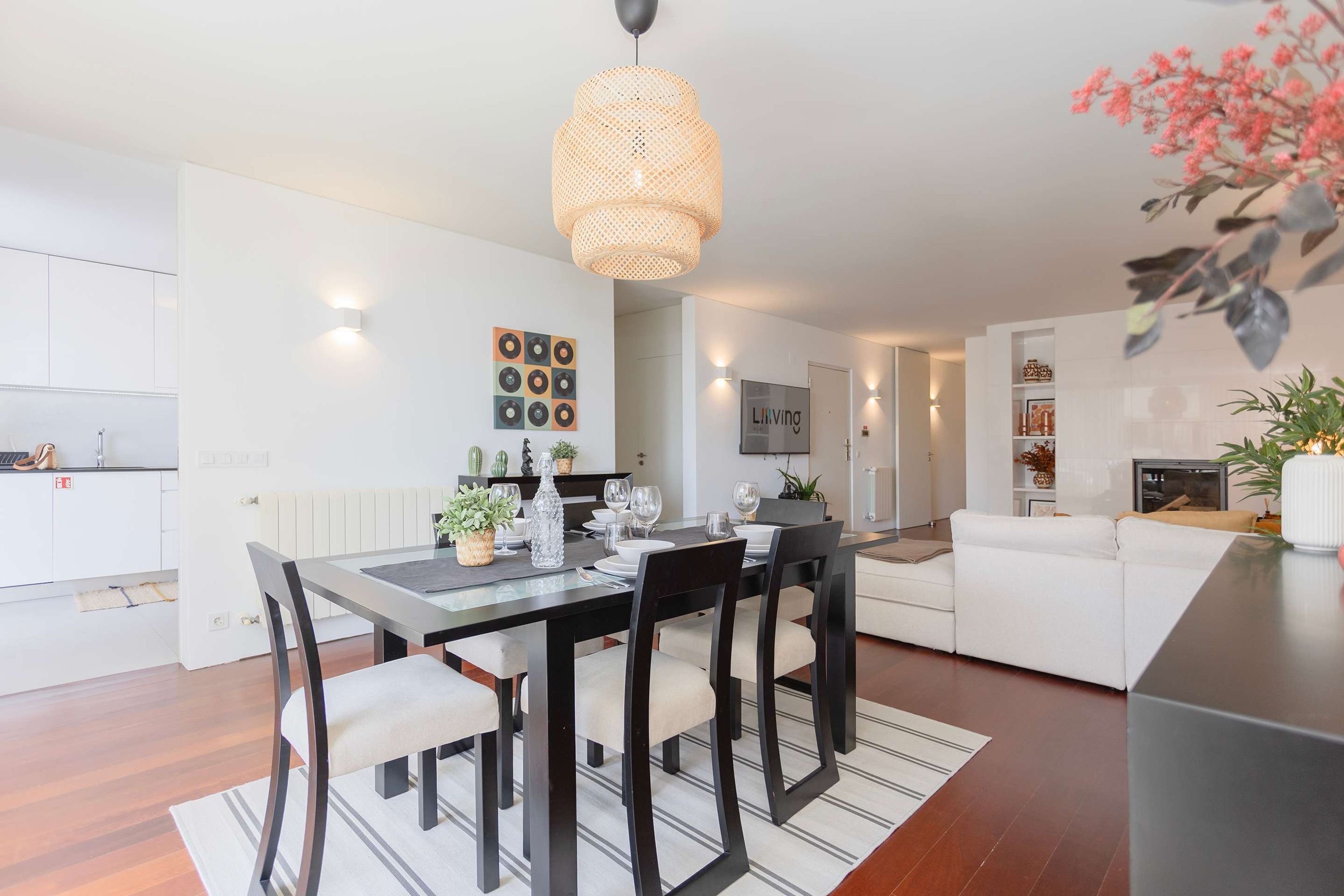 A modern living room with a dining area, white sofas, a black dining table, and a hanging light fixture.