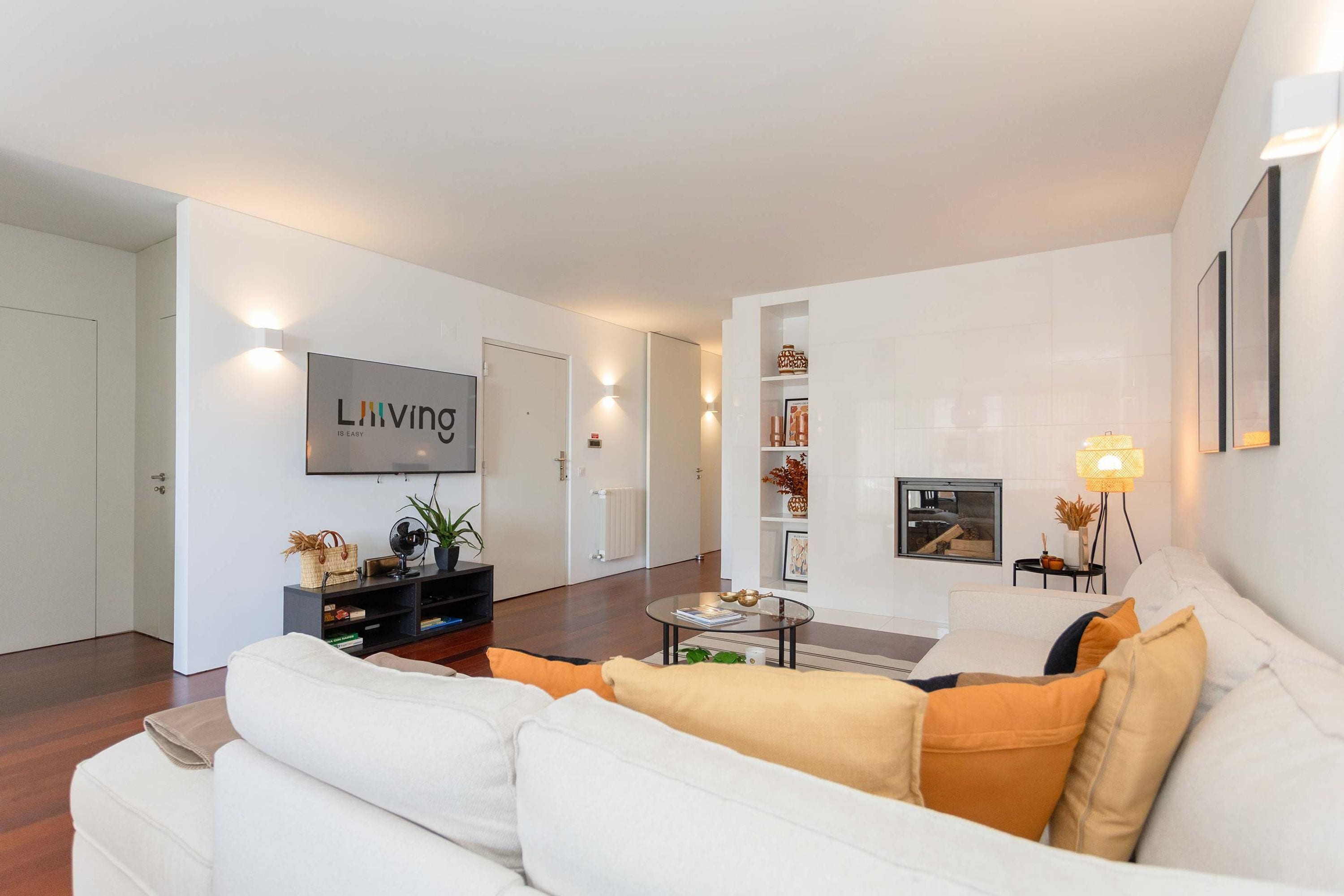 Una sala de estar moderna con un sofá blanco, una mesa de centro y un televisor montado en la pared.