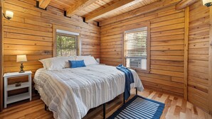 A wooden cabin bedroom with a bed, nightstands, and two windows. - Beautifully Renovated Property Just off Highway Close to Trails and Lead! (Lead)