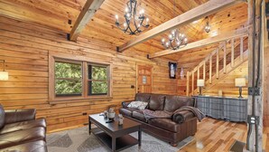 A log cabin interior with a leather sofa, a coffee table, and a staircase. - Beautifully Renovated Property Just off Highway Close to Trails and Lead! (Lead)