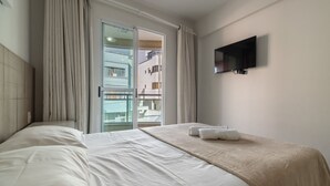 A hotel room with a bed, a TV mounted on the wall, and a view of the outside balcony. - RFO - Apartments Just Steps From Bombinhas Beach (Bombinhas)